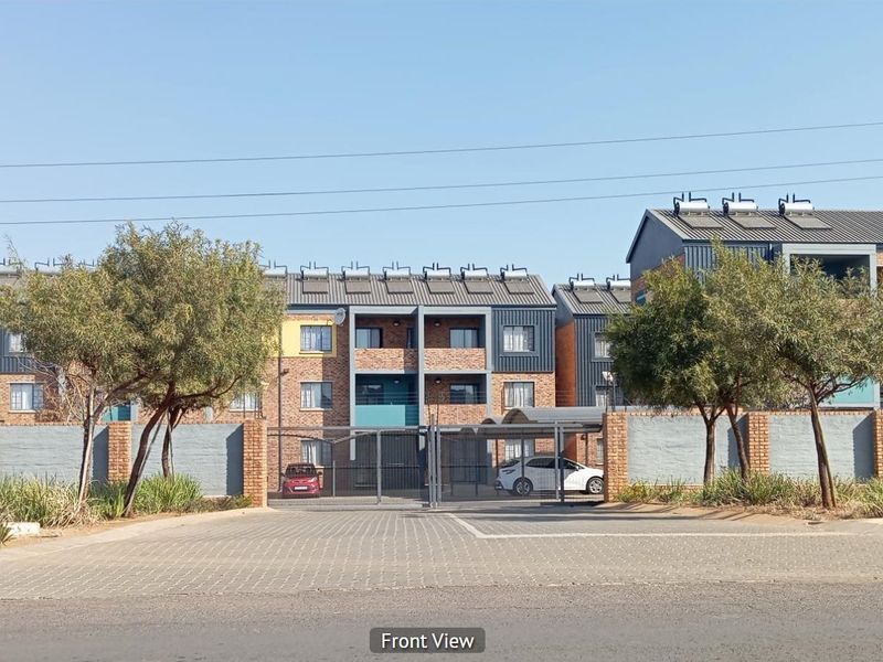 Front view of a multi-story apartment complex featuring brick facade, metal roofing with solar water heaters, and a secure gated entrance.