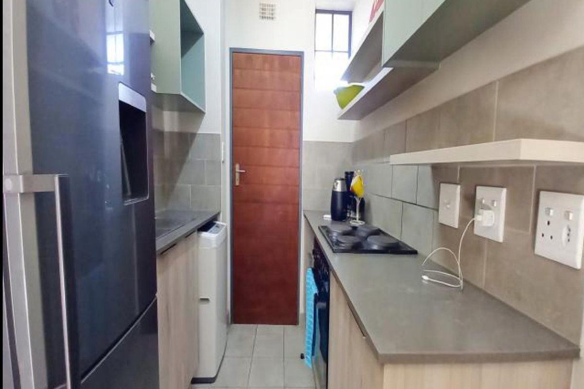 Compact galley-style kitchen featuring modern cabinetry, stone countertops, a built-in hob and oven, and neutral tiled finishes.