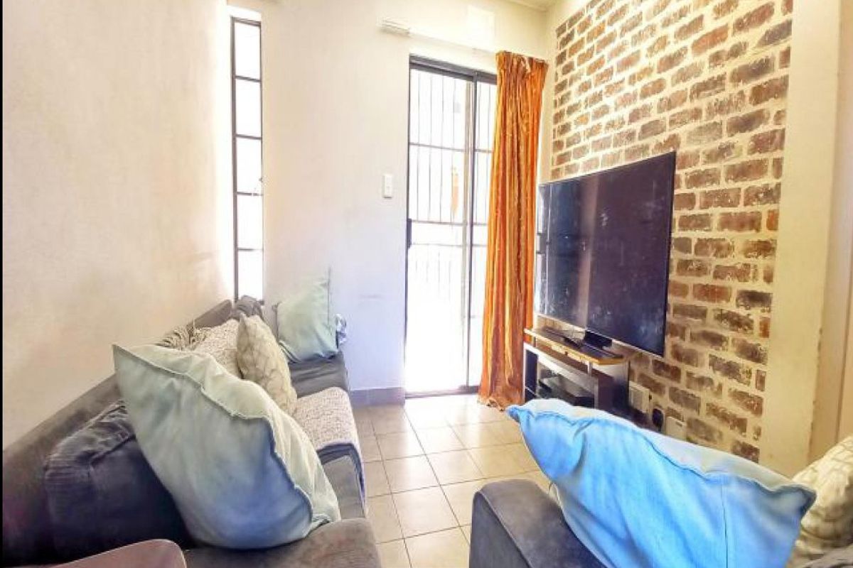 A living room featuring an exposed brick accent wall, tiled flooring, and a sliding glass door providing access to the exterior.