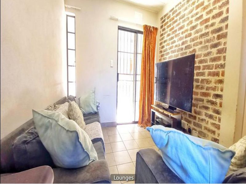 A living room featuring an exposed brick accent wall, tiled flooring, and a sliding glass door providing access to the exterior.