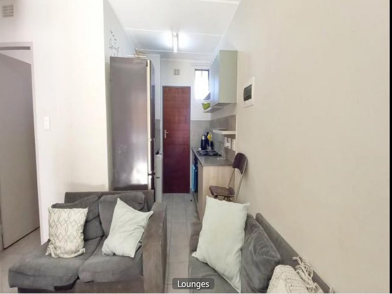 Compact open-plan living area featuring a kitchenette with built-in cabinetry and tiled flooring, suitable for efficient apartment living.