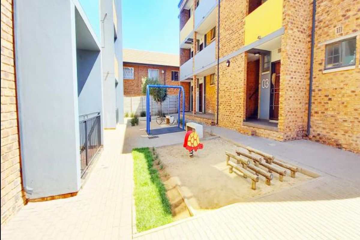A communal courtyard area featuring a sand pit and playground equipment situated between apartment building blocks.