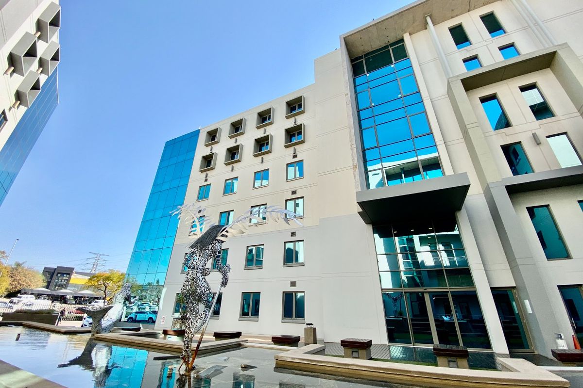 Modern commercial office building facade featuring extensive glass curtain walling, a prominent water feature, and contemporary architectural design elements.