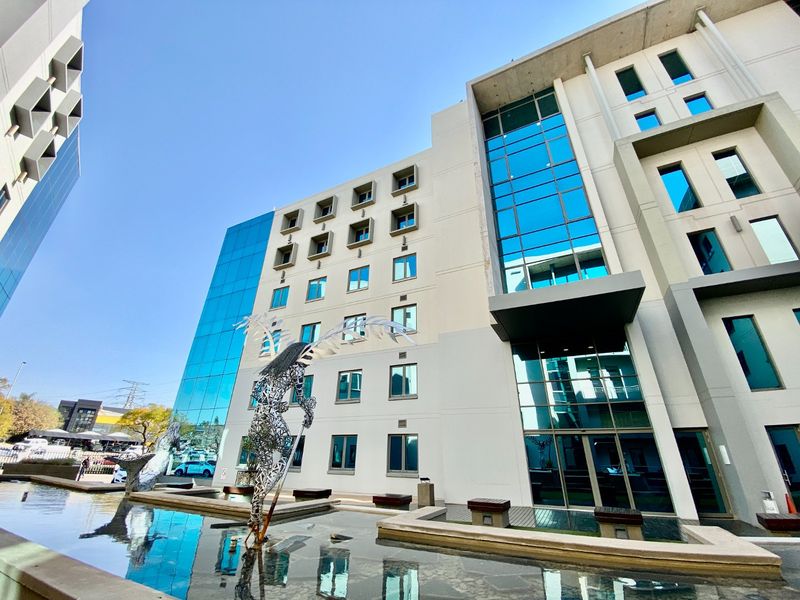 Modern commercial office building facade featuring extensive glass curtain walling, a prominent water feature, and contemporary architectural design elements.