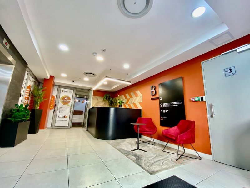 Modern commercial reception area featuring a sleek black desk, tiled flooring, and clear directional signage for building levels.