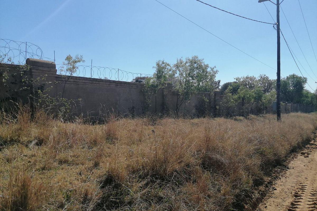 A view of the property boundary featuring a perimeter wall with razor wire, adjacent to an unpaved road and utility infrastructure.