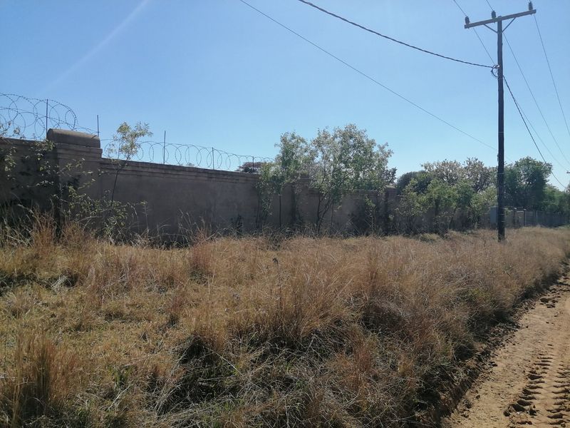 A view of the property boundary featuring a perimeter wall with razor wire, adjacent to an unpaved road and utility infrastructure.
