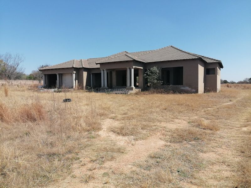 An unfinished single-story residential property featuring a tiled roof and concrete columns, currently in a shell state with no windows or doors installed.