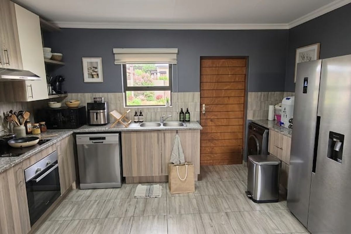 Modern kitchen featuring wood-grain cabinetry, laminate countertops, built-in oven, extractor fan, and integrated laundry space with tiled flooring and backsplash.
