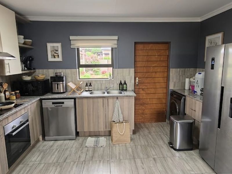 Modern kitchen featuring wood-grain cabinetry, laminate countertops, built-in oven, extractor fan, and integrated laundry space with tiled flooring and backsplash.