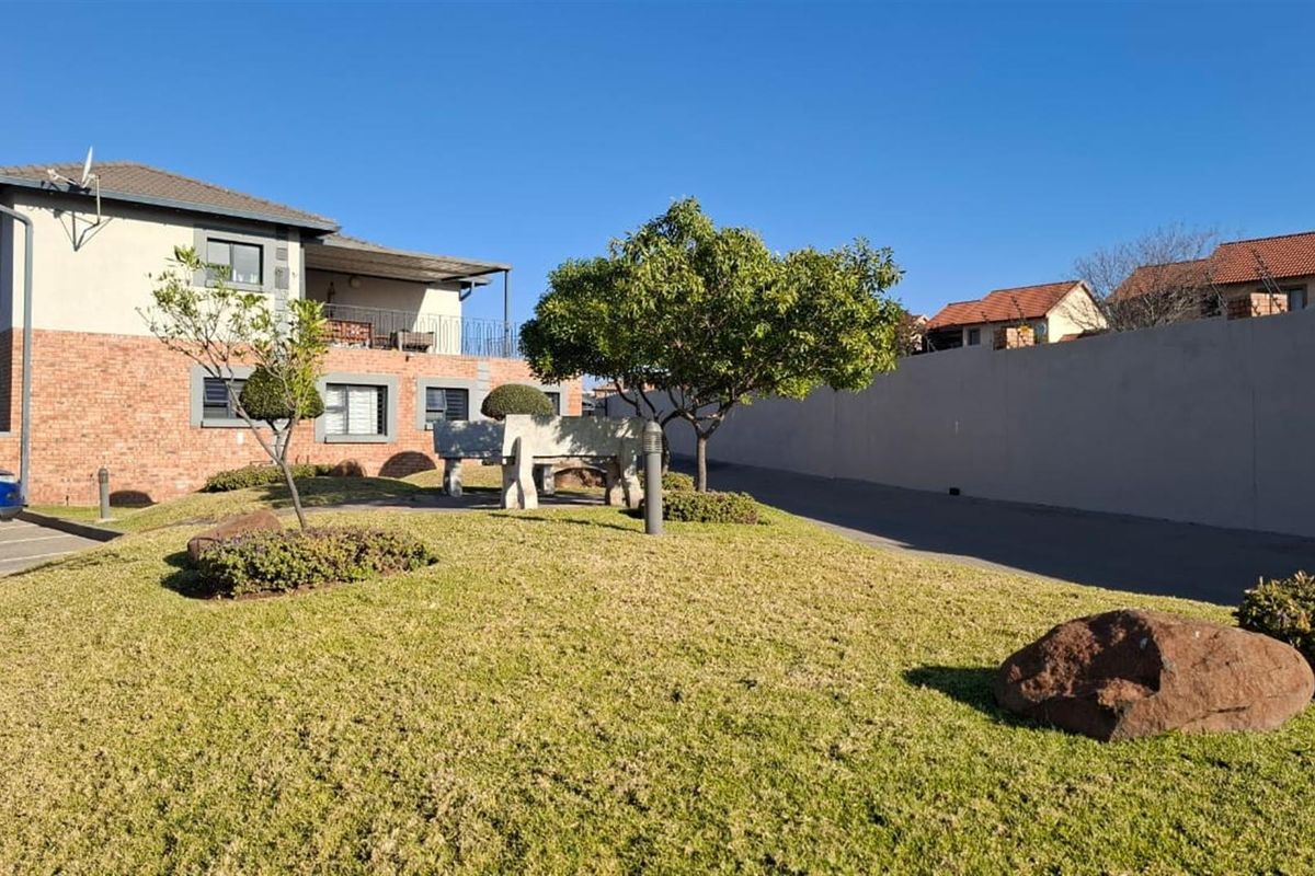 A well-maintained exterior view of the apartment complex featuring a brick facade, paved driveway, and landscaped garden area.