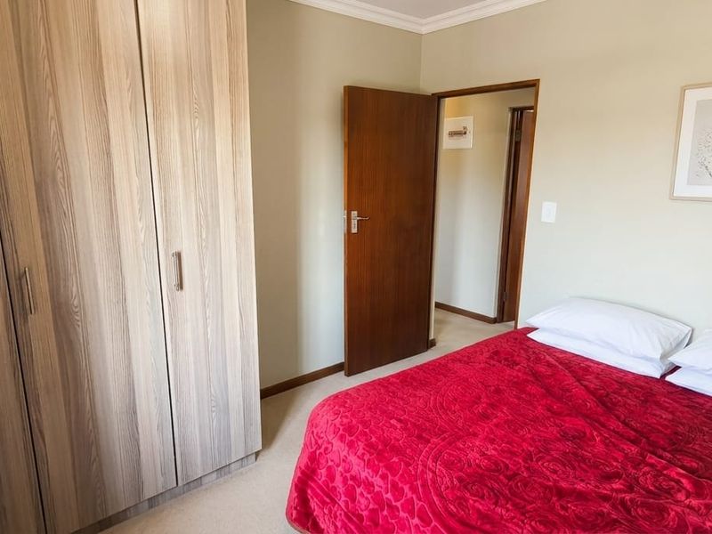 A well-maintained bedroom featuring neutral wall tones, carpeted flooring, and a large built-in wooden wardrobe.