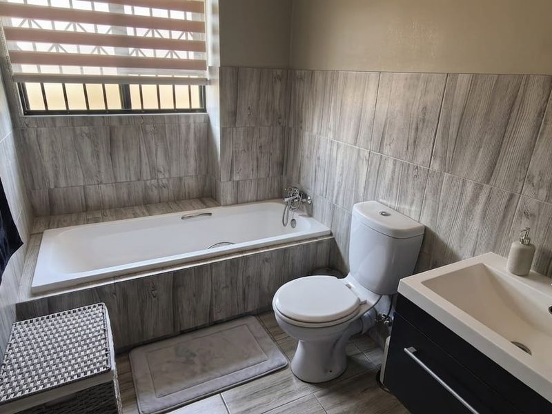 A modern bathroom featuring wood-look wall tiles, a built-in bathtub, a white toilet, and a contemporary vanity unit with a basin.