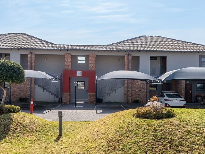 Front elevation of a modern apartment complex featuring brick and plaster finishes, covered parking bays, and well-maintained landscaped grounds.