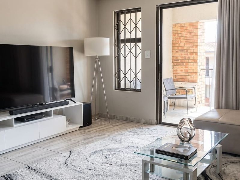 A well-maintained living room featuring tiled floors, security bars on the window, and direct access to an outdoor balcony area.