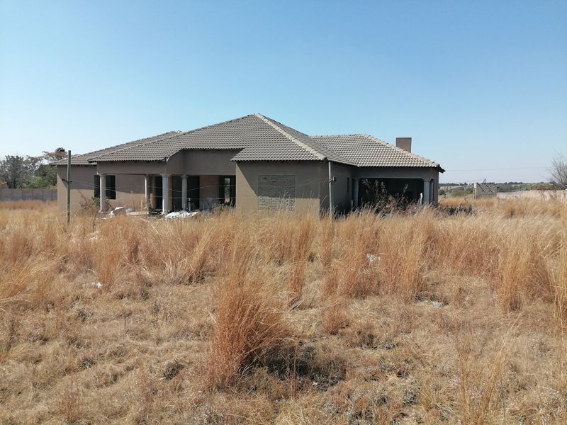 An unfinished residential property structure set on a large plot of land with overgrown grass and clear signs of incomplete construction.