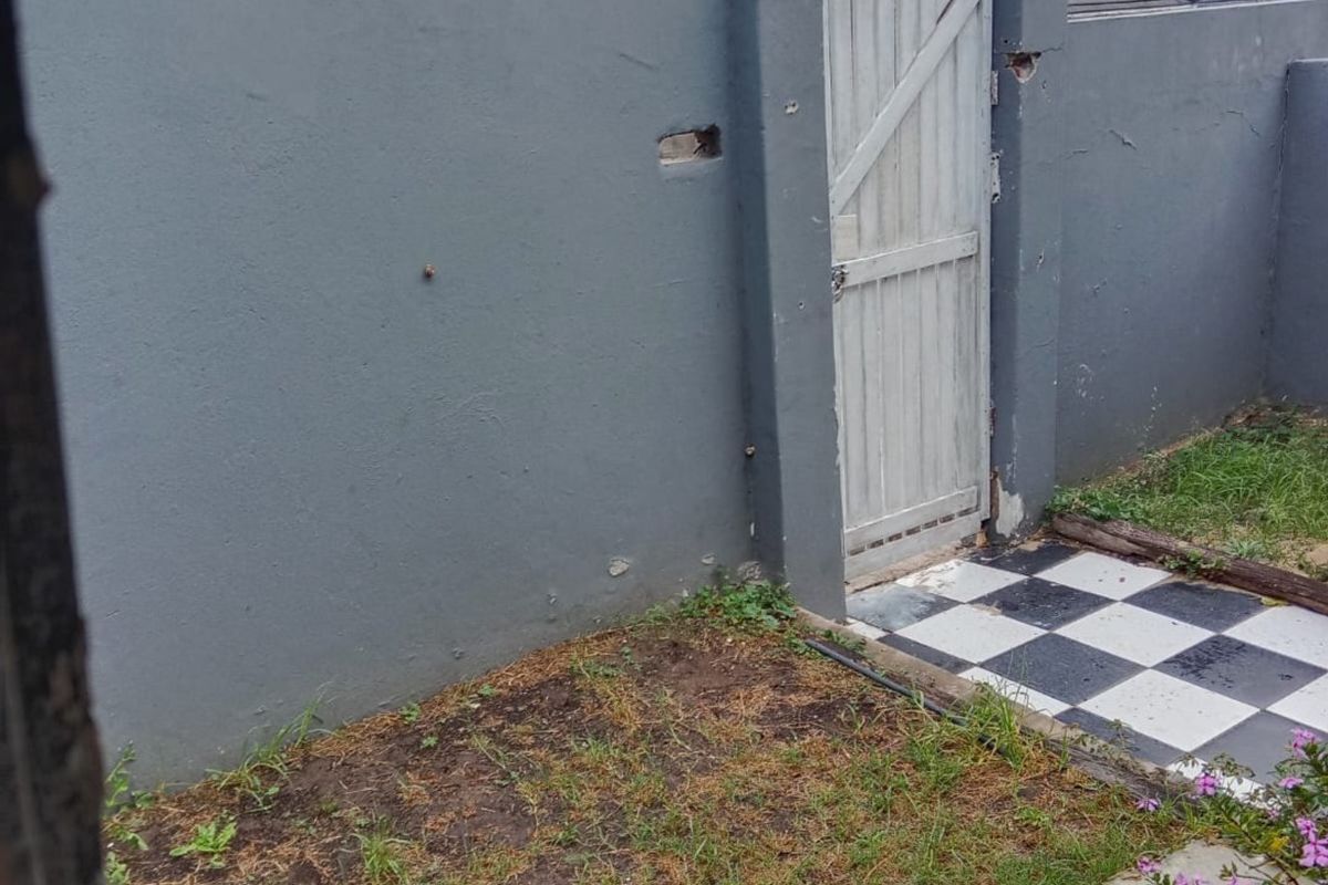 A rear exterior view of a townhouse featuring a boundary wall with a pedestrian gate and a checkered tile pathway.