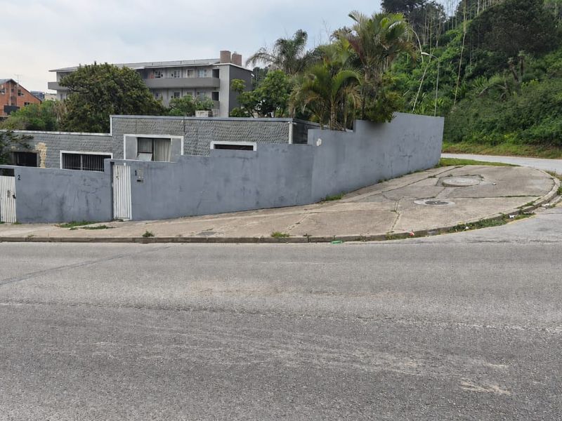 Street view of the property showing the exterior perimeter wall, security gate, and concrete driveway area.