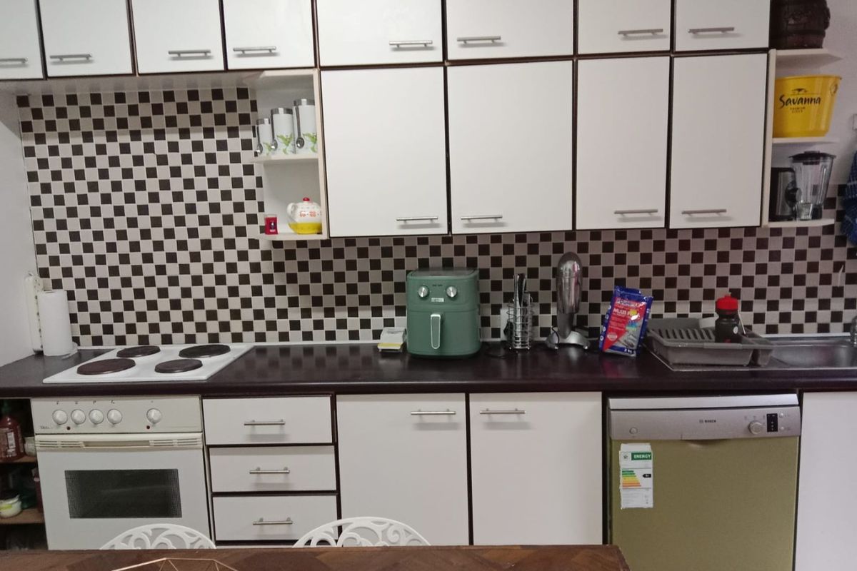 A functional kitchen featuring white cabinetry, a dark laminate countertop, a checkered tile backsplash, and built-in appliances including an oven, hob, and dishwasher.
