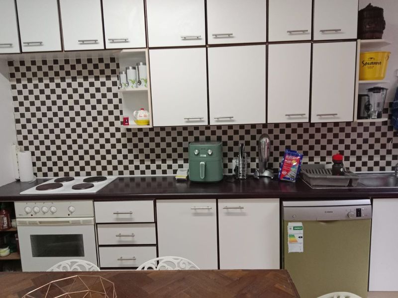 A functional kitchen featuring white cabinetry, a dark laminate countertop, a checkered tile backsplash, and built-in appliances including an oven, hob, and dishwasher.