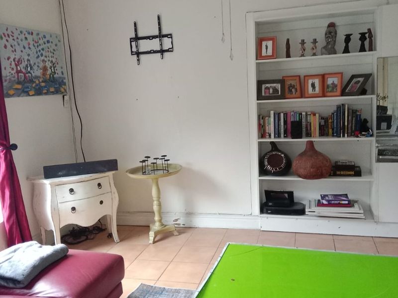 A living room featuring a built-in shelving unit, tiled flooring, and a wall-mounted television bracket, offering a functional space for relaxation.