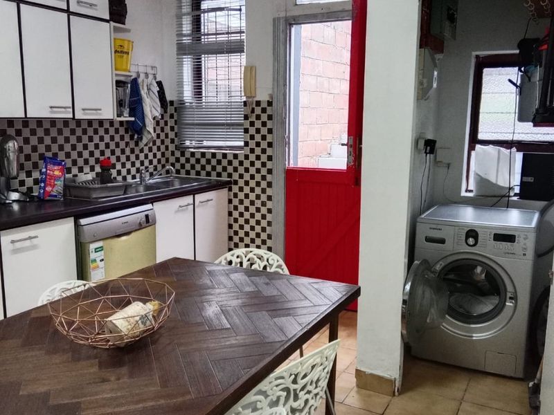 A functional kitchen featuring built-in cabinetry, tiled backsplash, and an adjoining laundry area with direct access to the exterior.