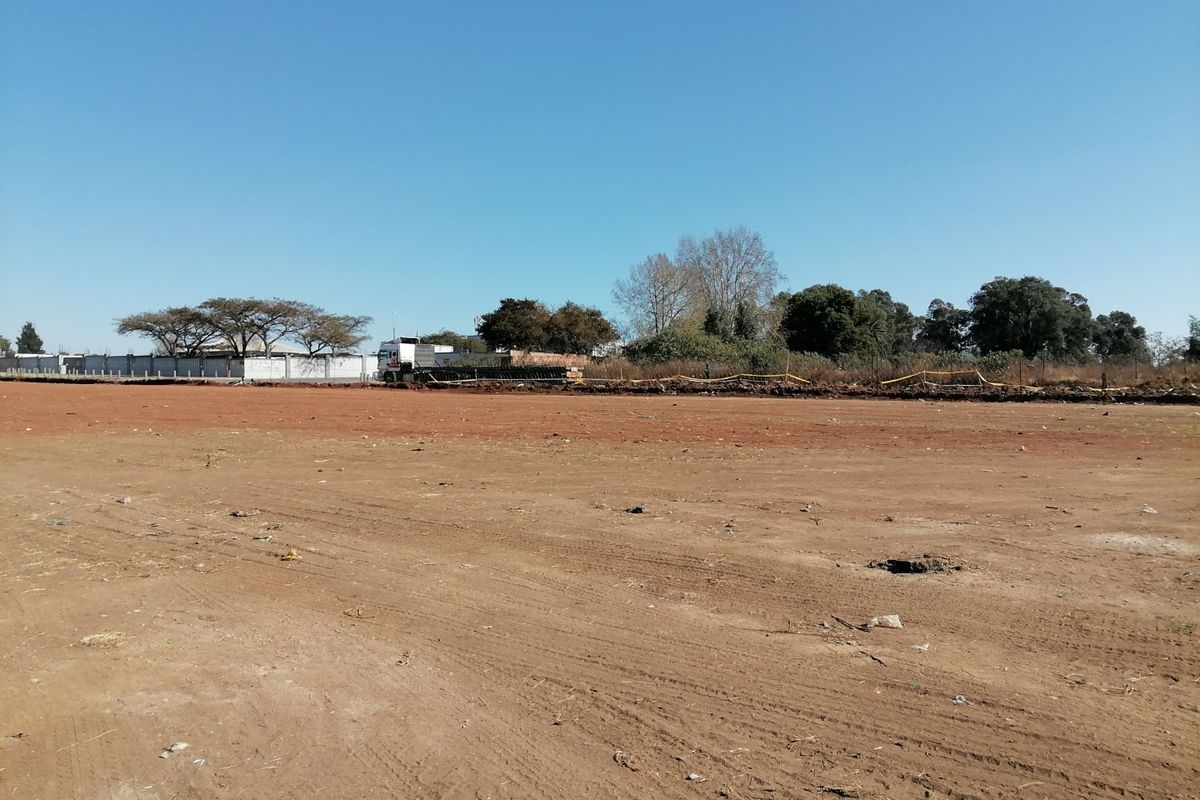 A wide-angle view of a vacant residential plot featuring cleared earth and perimeter fencing, ready for development.