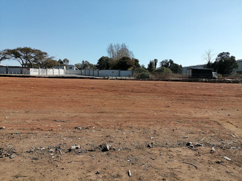 A wide, level vacant residential plot featuring cleared red earth, enclosed by a perimeter wall and fencing.