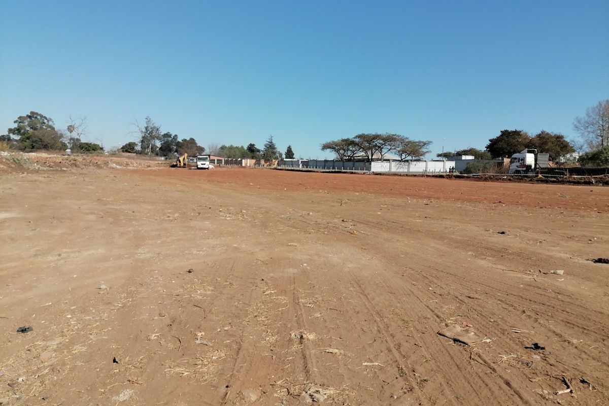 A wide-angle view of a cleared, vacant residential plot of land with perimeter fencing visible in the background.