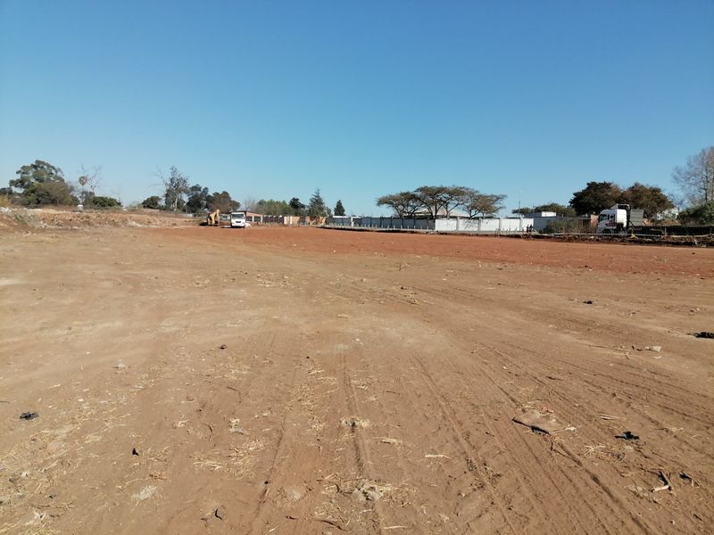 A wide-angle view of a cleared, vacant residential plot of land with perimeter fencing visible in the background.