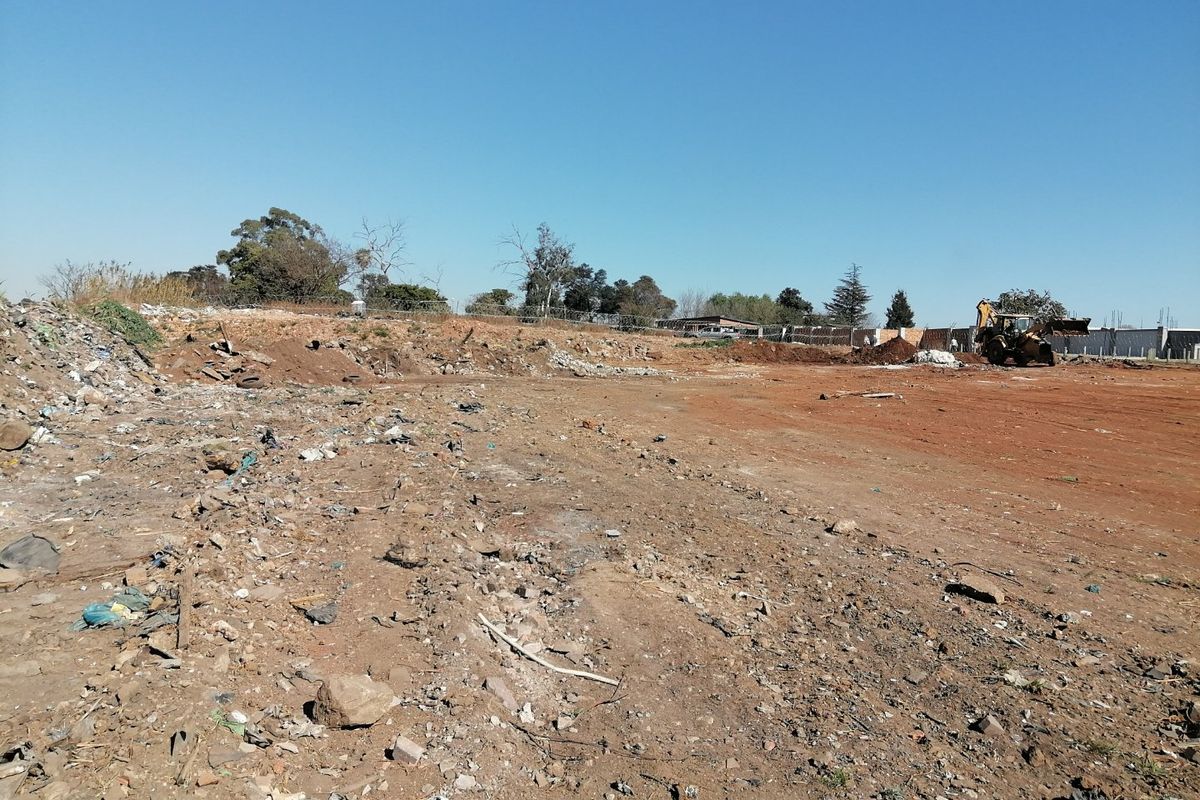 A wide view of a vacant residential plot featuring cleared earth and perimeter fencing, currently containing scattered debris.