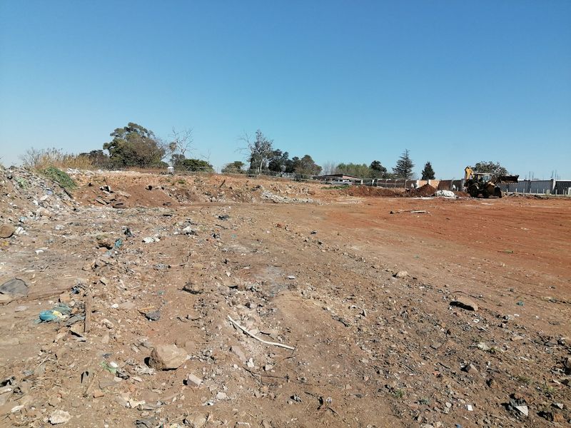 A wide view of a vacant residential plot featuring cleared earth and perimeter fencing, currently containing scattered debris.