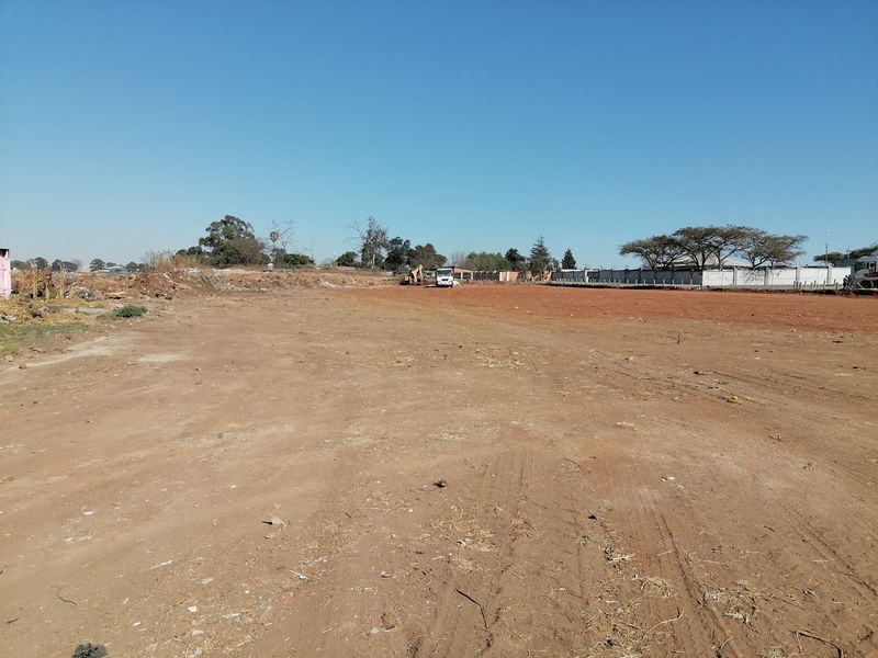 A wide-angle view of a vacant residential plot of land, featuring cleared ground and perimeter boundary walls.