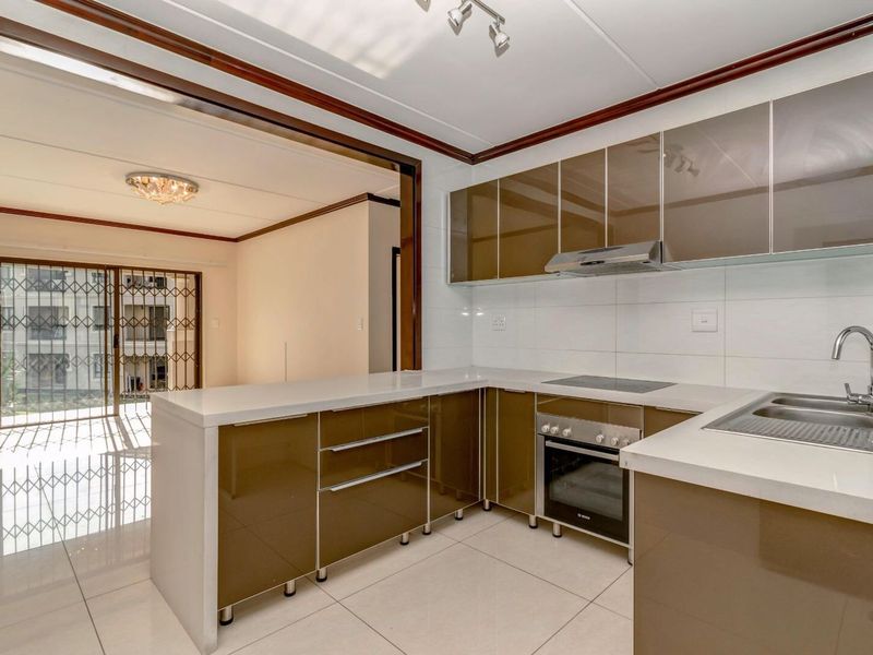 Modern open-plan kitchen featuring high-gloss cabinetry, stone countertops, integrated appliances, and tiled flooring, seamlessly flowing into the adjacent living area.