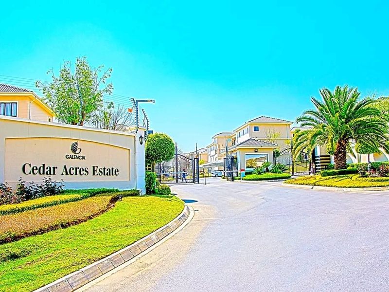 The entrance to Cedar Acres Estate featuring a secure gated access point, manicured landscaping, and paved driveway infrastructure.