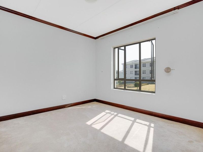 A bright, empty bedroom featuring neutral carpeting, timber crown molding, and large casement windows providing natural light.
