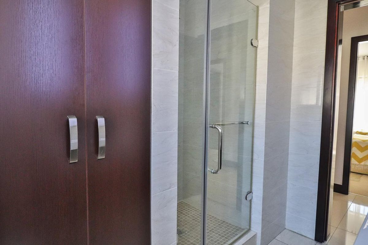 A clean bathroom featuring a glass-enclosed shower, neutral wall tiling, and dark wood-finish built-in cabinetry.