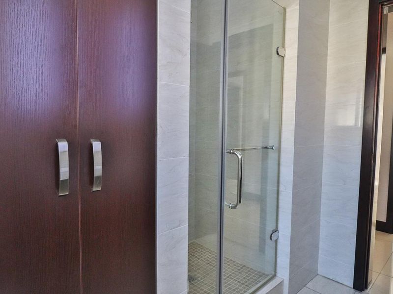 A clean bathroom featuring a glass-enclosed shower, neutral wall tiling, and dark wood-finish built-in cabinetry.