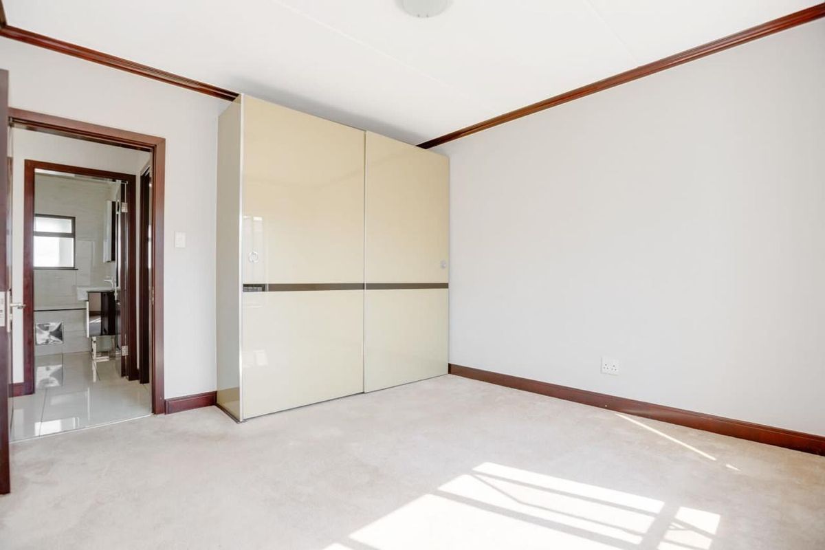 A bright, empty bedroom featuring neutral carpeting, dark wood trim, and a large built-in wardrobe with sliding doors.