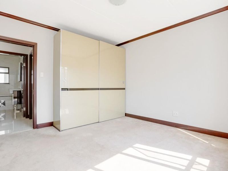 A bright, empty bedroom featuring neutral carpeting, dark wood trim, and a large built-in wardrobe with sliding doors.