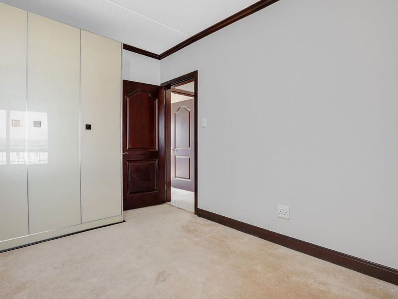 A clean, empty bedroom featuring built-in cupboards, carpeted flooring, and classic timber trim details throughout the space.