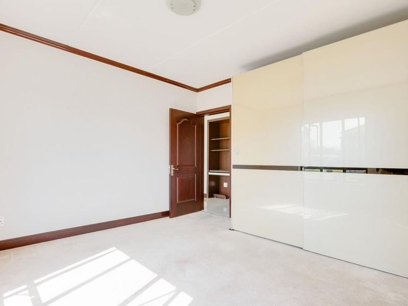 A bright, empty bedroom featuring neutral carpeting, crown molding, and a large, modern built-in sliding door wardrobe.