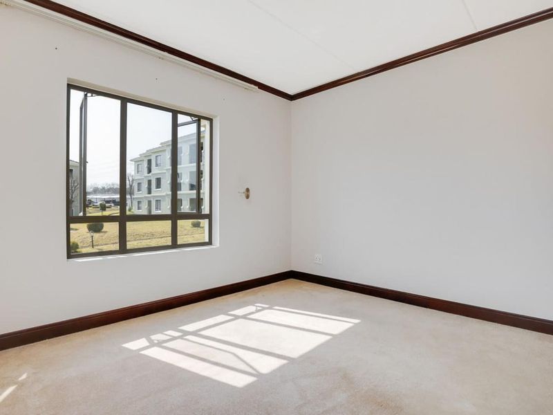 A vacant bedroom featuring neutral carpet flooring, dark timber crown molding, and large aluminium-framed windows providing natural light.