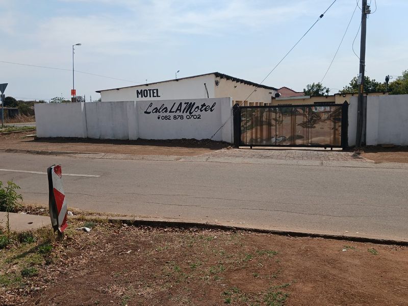 Front exterior view of a commercial motel property featuring a perimeter wall, gated entrance, and signage visible from the street.