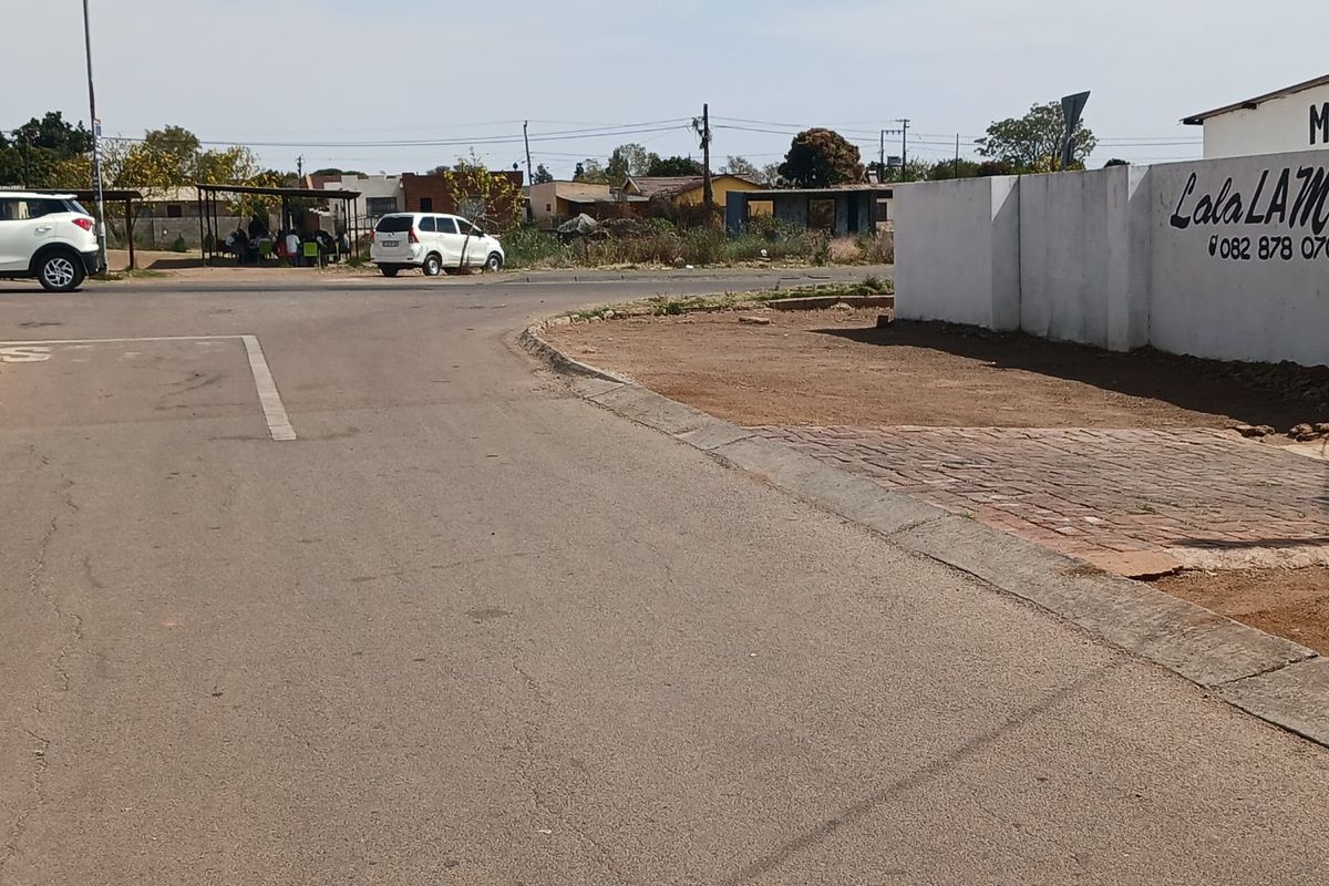 Street view showing the property boundary wall, paved driveway entrance, and adjacent asphalt road infrastructure.