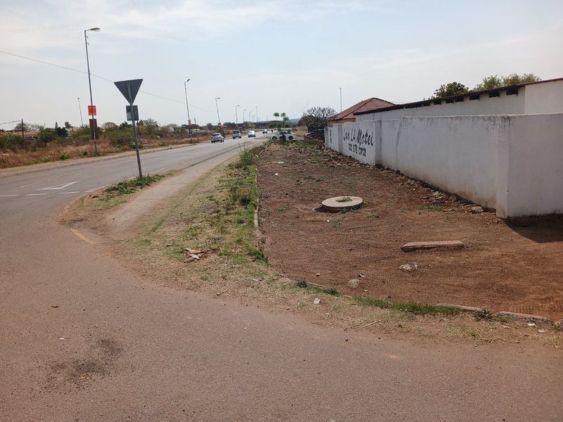 Street view showing the roadside verge, boundary wall of the commercial property, and adjacent public road infrastructure.