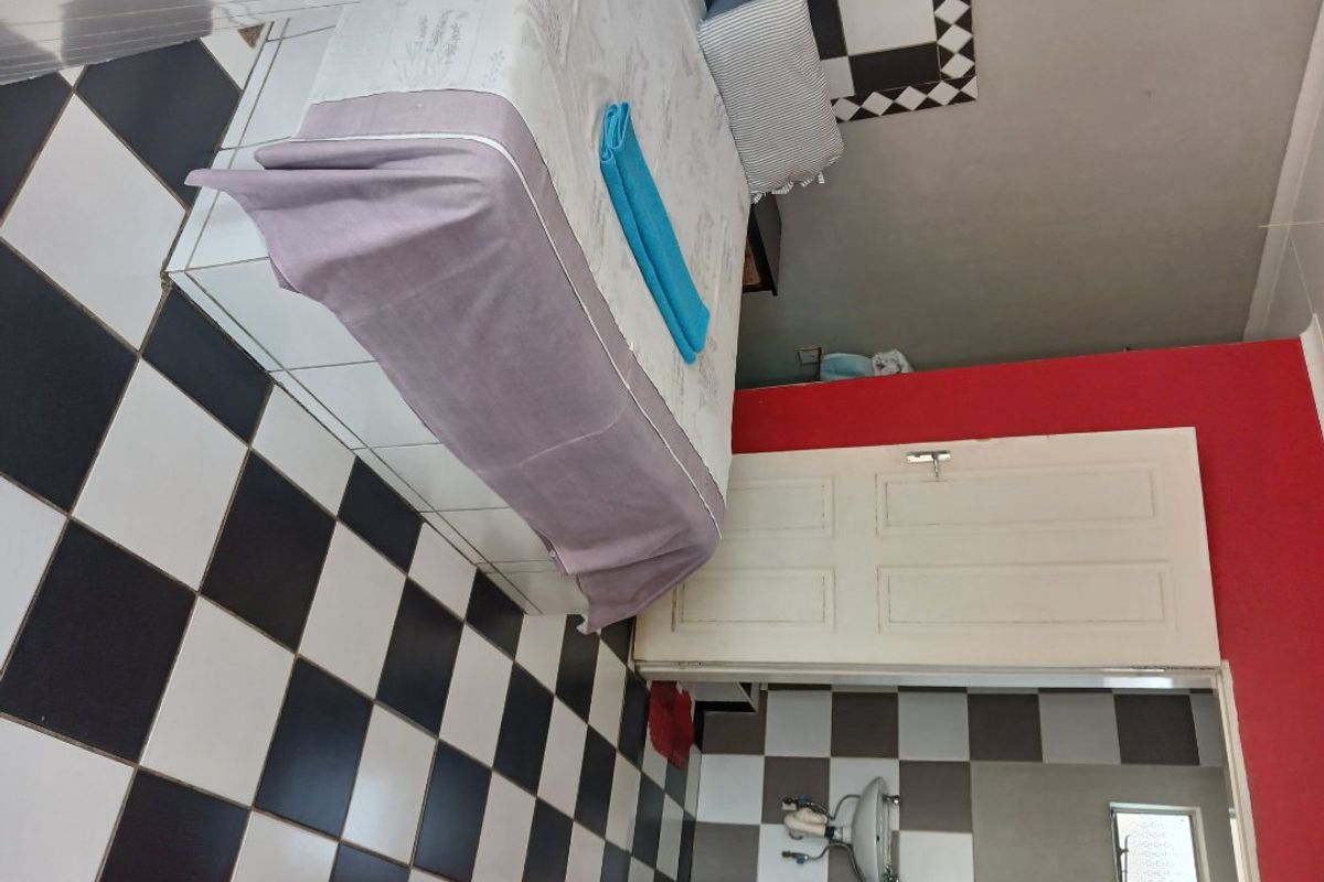 A bedroom featuring black and white checkered floor tiles, a wall-mounted basin, and a panel door, requiring cosmetic updates and maintenance.