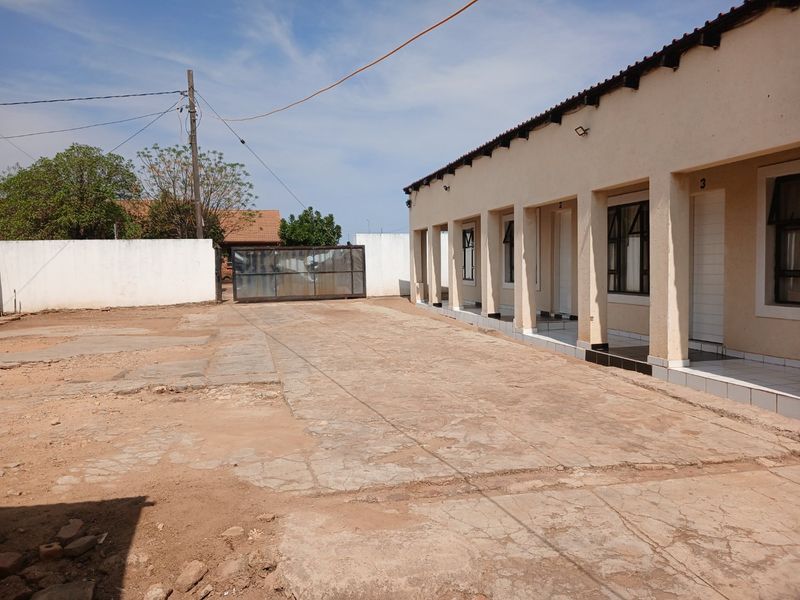 Rear exterior view of a commercial property featuring a concrete paved yard, perimeter wall, and a row of units with a covered walkway.