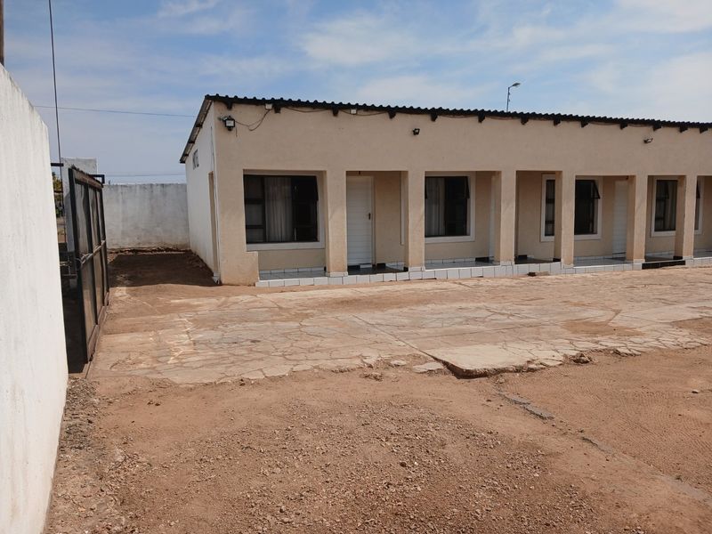 Front exterior view of a commercial building featuring a covered patio, tiled walkway, and a large concrete driveway area requiring maintenance.