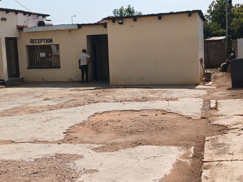 Exterior view of a commercial reception area featuring a paved courtyard with significant surface damage and weathered building finishes.